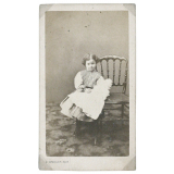 Petite fille à la poupée, s'appuyant à une chaise. 