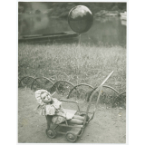 Poussette-jouet sur laquelle est posée une poupée et à laquelle est accroché un ballon. 