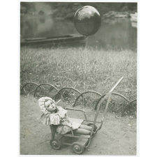 Poussette-jouet sur laquelle est posée une poupée et à laquelle est accroché un ballon.