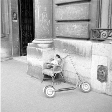 Rentrée scolaire, 1956 : des jouets. Une trottinette, un fauteuil en rotin d'enfant sur lequel est posé un fauteuil de poupée et sa poupée