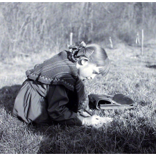 Ecole Freinet, classe promenade : une écolière, assise dans l'herbe, rédige sur une feuille.
