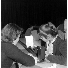 Collège d'enseignement technique pour jeunes filles. Deux élèves, sous la surveillance de leur enseignante, observent des lentilles convergentes.