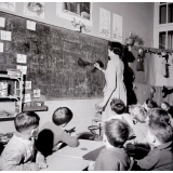 Méthode Freinet : l'apprentissage de l'imprimerie et la réalisation d'un journal scolaire. La maîtresse écrit un texte au tableau noir.