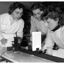 Collège d'enseignement technique pour jeunes filles. Deux élèves, sous la surveillance de leur enseignante, observent des lentilles convergentes.