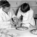 Collège d'enseignement technique pour jeunes filles. Le cours de cuisine. Le professeur guide une élève pour la décoration d'un plat.