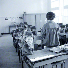 Ecole primaire. L'institutrice, en blouse, vérifie les ardoises.