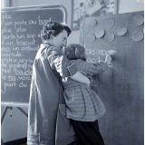 Ecole primaire. L'institutrice aide une élève à écrire au tableau.