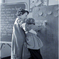 Ecole primaire. L'institutrice aide une élève à écrire au tableau.