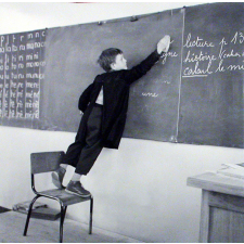 Ecole primaire. Un élève, juché sur une chaise, efface le tableau noir
