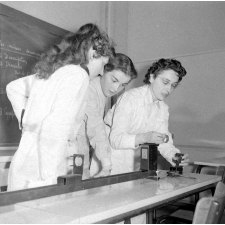 Collège d'enseignement technique pour jeunes filles. Deux élèves, sous la surveillance de leur enseignante, observent des lentilles convergentes.