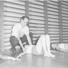 Service de la jeunesse et des sports : la rééducation neuro-motrice. Des jeunes filles pratiquent des exercices d'assouplissement sous le contrôle d'un éducateur.