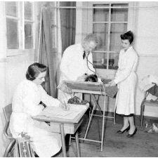 Visite médicale (cabinet mobile) à l'école primaire de Labruguière. L'auscultation d'un élève par le médecin scolaire assisté de deux infirmières. Table d'examen et isoloirs portatifs.