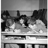 Enseignement audio-visuel. Une classe en activité. Deux garçons écrivent. L'un porte une blouse.