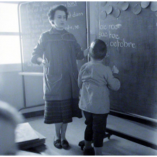Ecole primaire. L'institutrice aide un élève à écrire au tableau.
