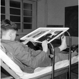 Centre de réadaptation fonctionnelle : un élève alité feuillette un livre de photographies. 
