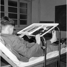 Centre de réadaptation fonctionnelle : un élève alité feuillette un livre de photographies. 