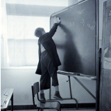 Ecole primaire. Un élève, juché sur une chaise, efface le tableau.