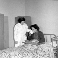 Collège d'enseignement technique pour jeunes filles. L'infirmière amène un plateau à une élève couchée à l'infirmerie.