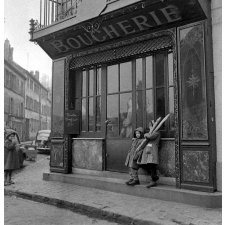 Rentrée scolaire à Paris : des enfants dans la rue, devant une boucherie ; l'un d'eux tenant deux baguettes de pain