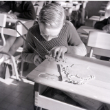 Méthode Freinet, classe promenade : travaux manuels éducatifs. Un garçon découpe un  puzzle à la scie. 